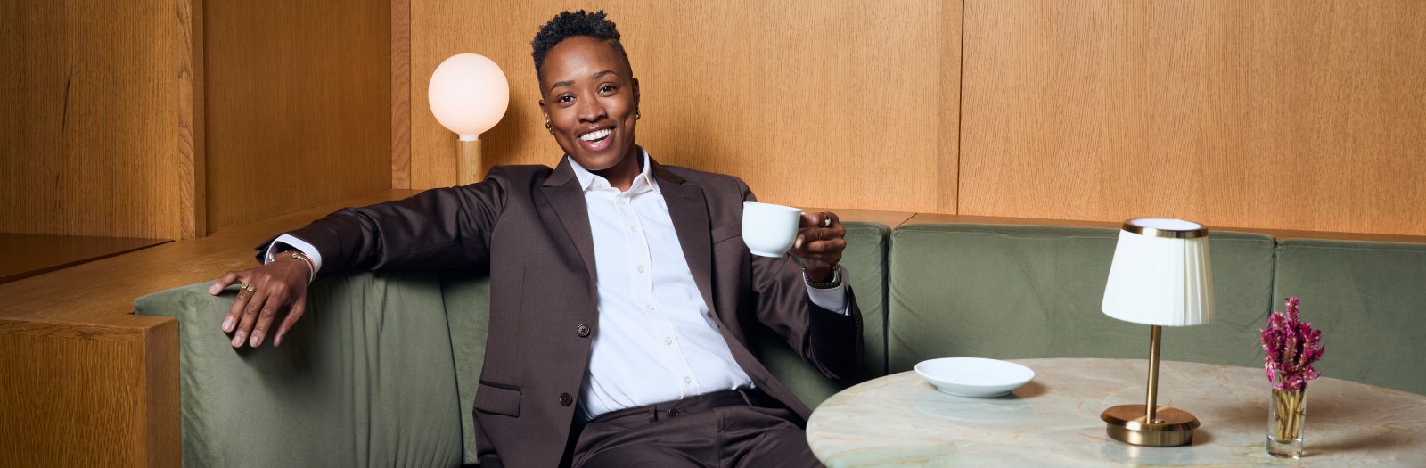 Model in chocolate Georgie suit sitting with a coffee cup in their hand.