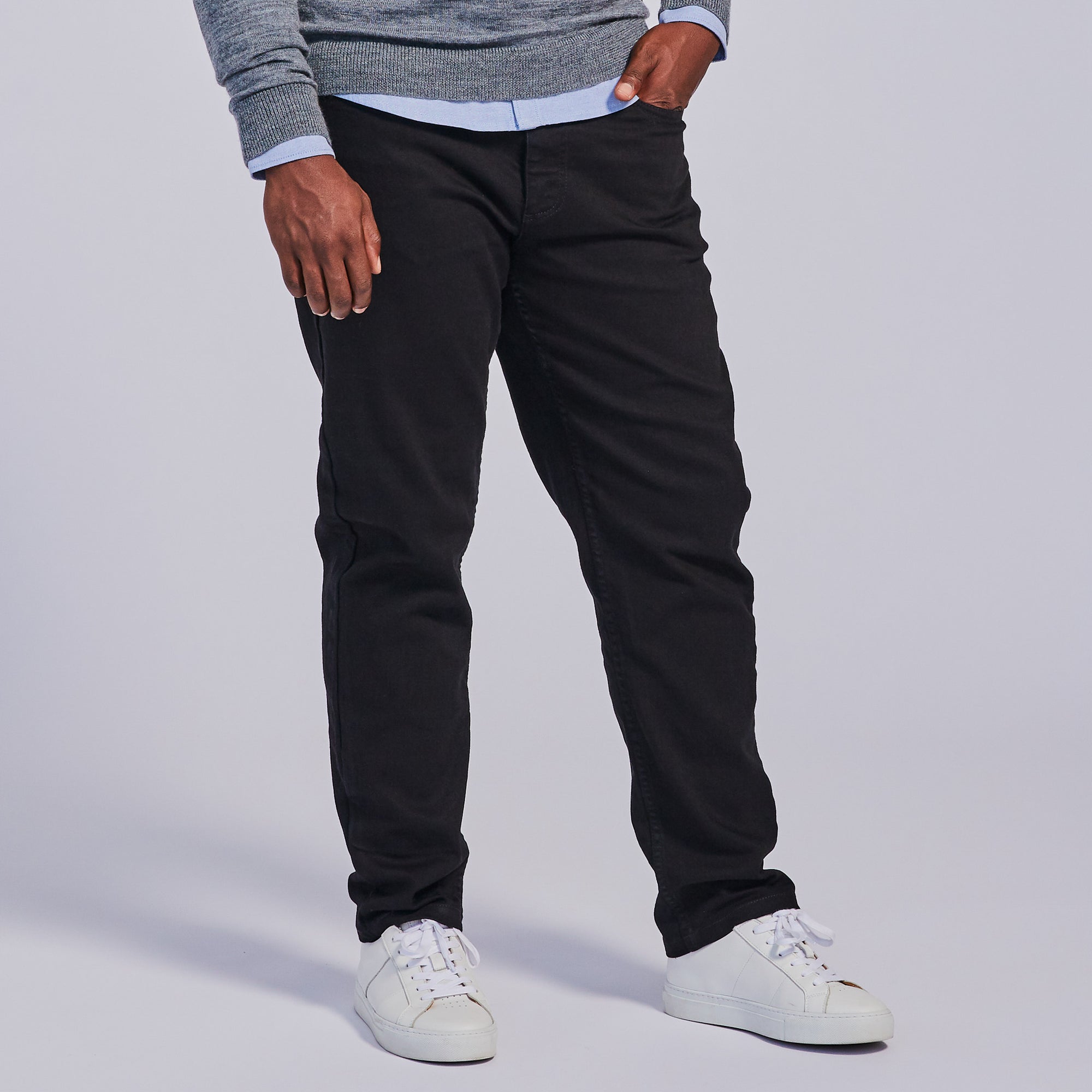 A person standing against a plain background, wearing slim-tapered black jeans and white sneakers. Color: Black