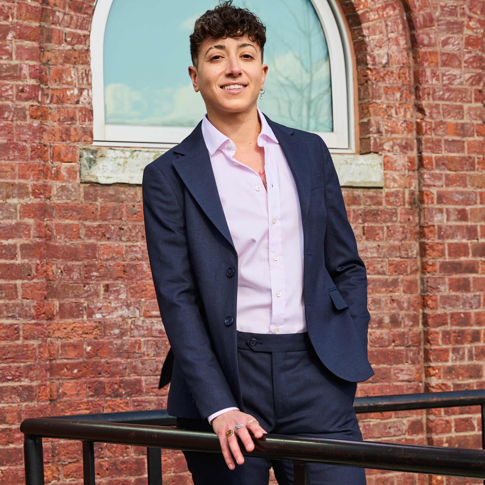 Model wearing The Scout Ink Blue Suit Blazer made by Kirrin Finch standing against a brick wall. Color: Ink Blue