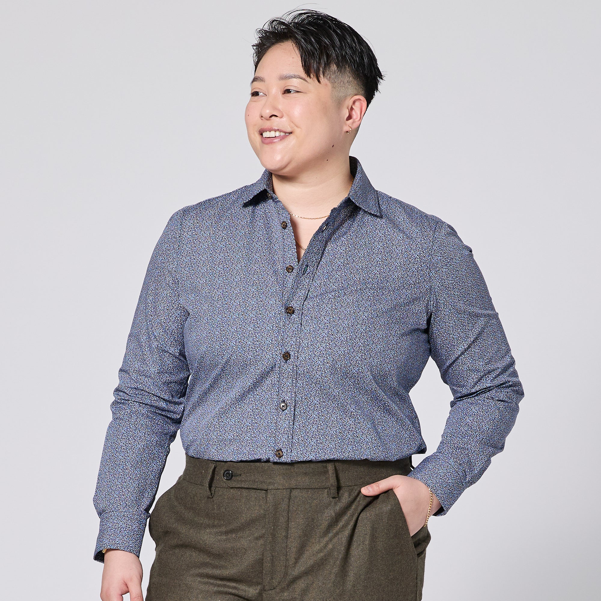 Person wearing a blue patterned shirt and brown pants on a light gray background. Color: Murano 