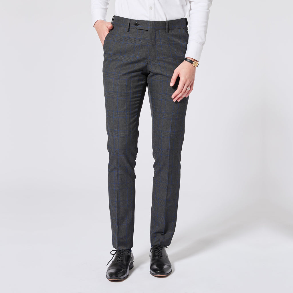 A person wearing slim-fit dark gray plaid trousers, a white long-sleeve shirt, and black leather dress shoes, standing against a light gray studio background. Color: Gray Admiral Plaid