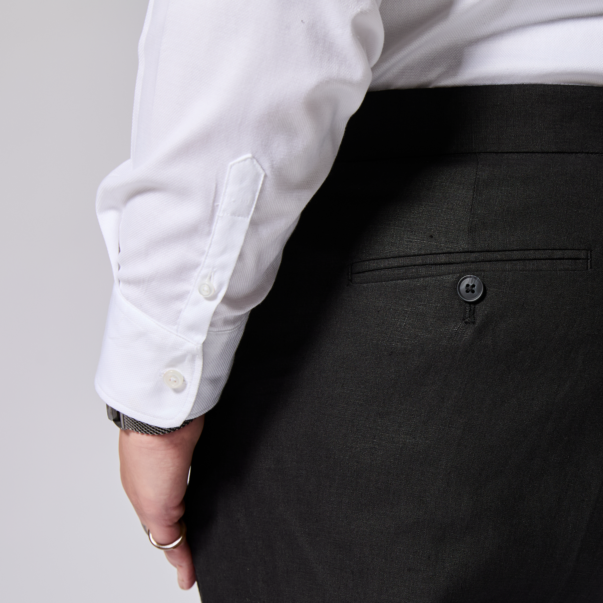 Person wearing a white shirt and black pants on a plain background. Color: Black