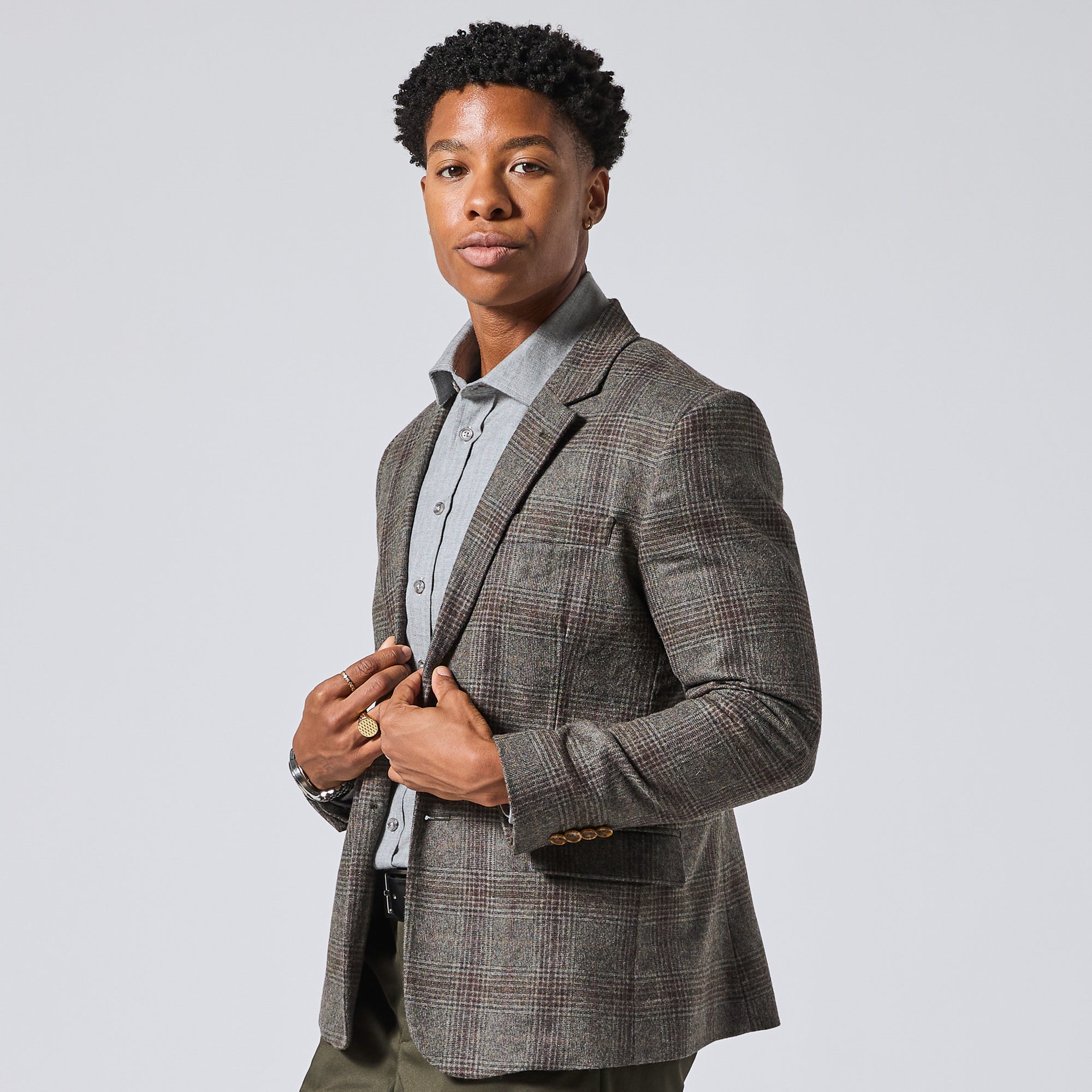 Model wearing a gray and brown plaid blazer over a light gray dress shirt, standing against a solid light gray background. Color: Earthen Glen Plaid
