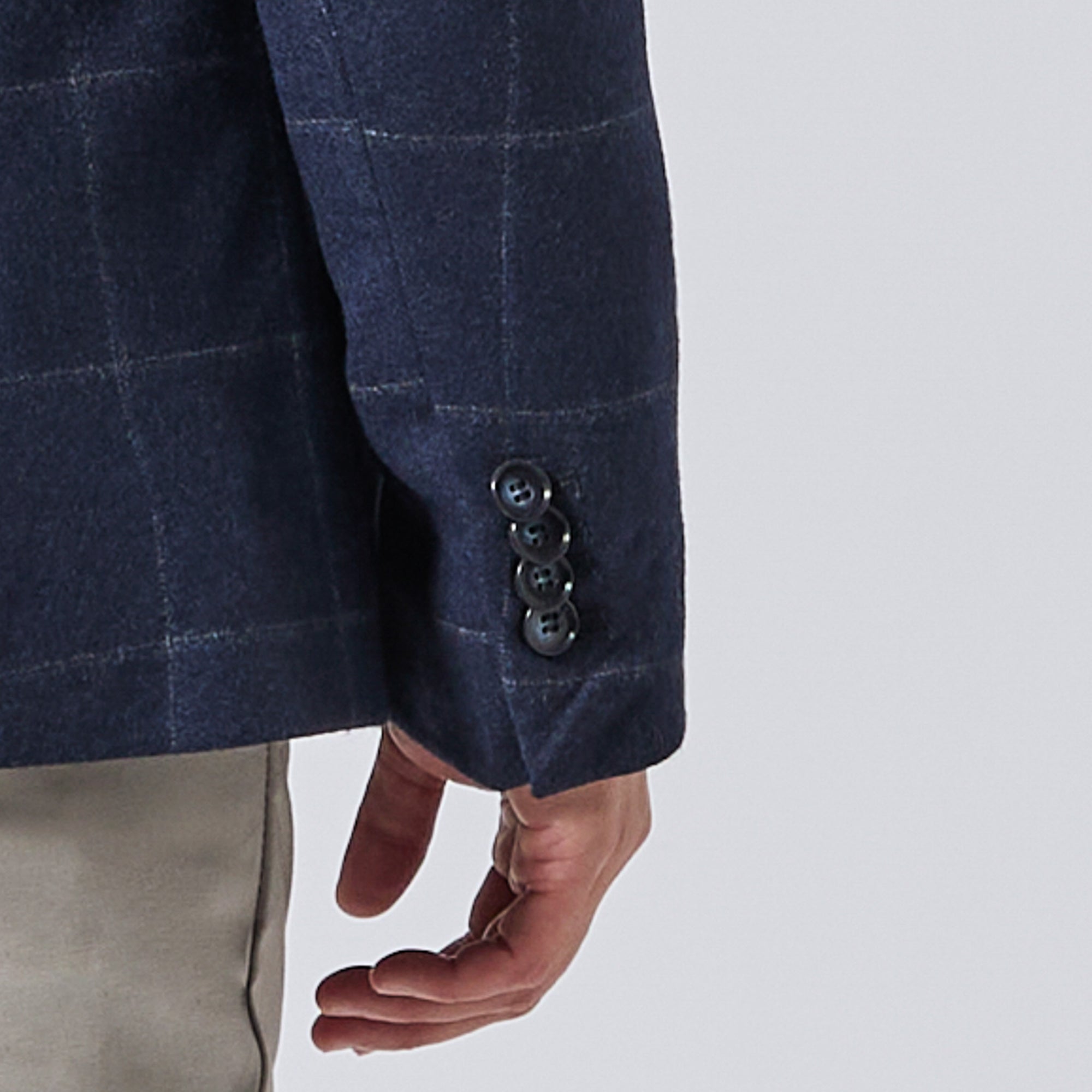 Close-up of a navy blue windowpane plaid blazer sleeve with four dark buttons, worn by a model with beige trousers against a light gray background. Color: Navy Regatta