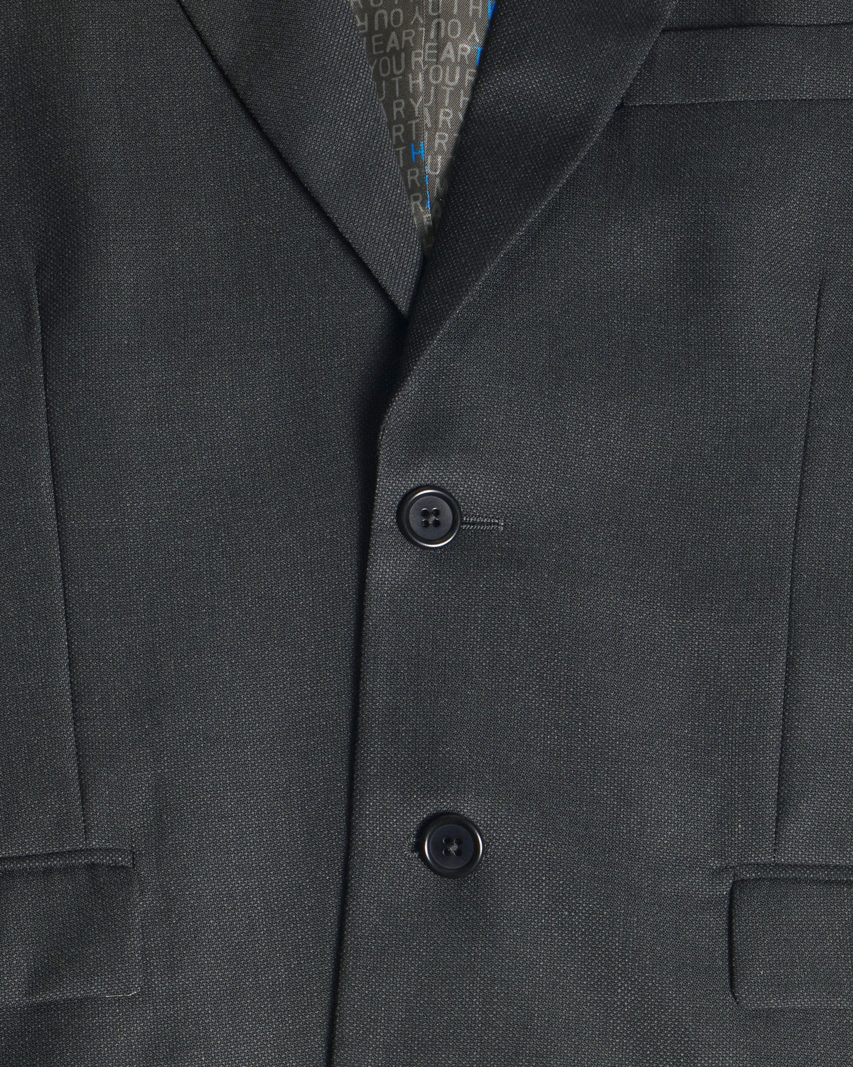 Close-up of a dark charcoal gray suit jacket with two buttons, showing the fine twill texture of the fabric and a patterned inner collar lining. Color: Nightfall Birdseye