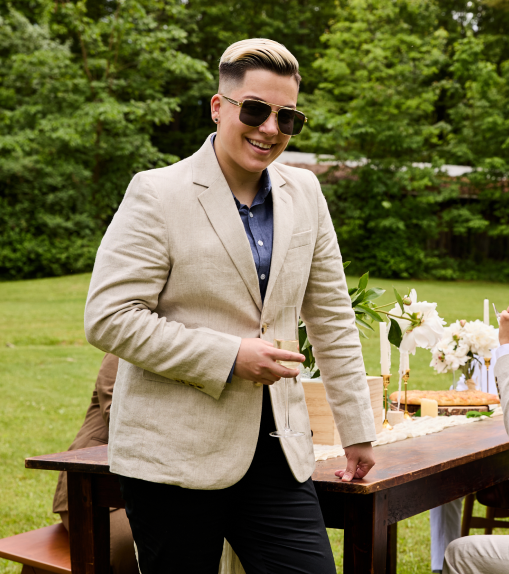 Person in a beige linen blazer standing outdoors near a table with floral arrangements.