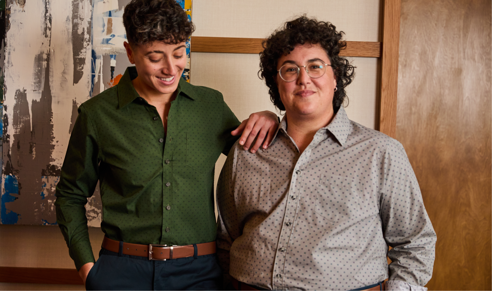 Two people standing together with one person's arm on the others, indoors.