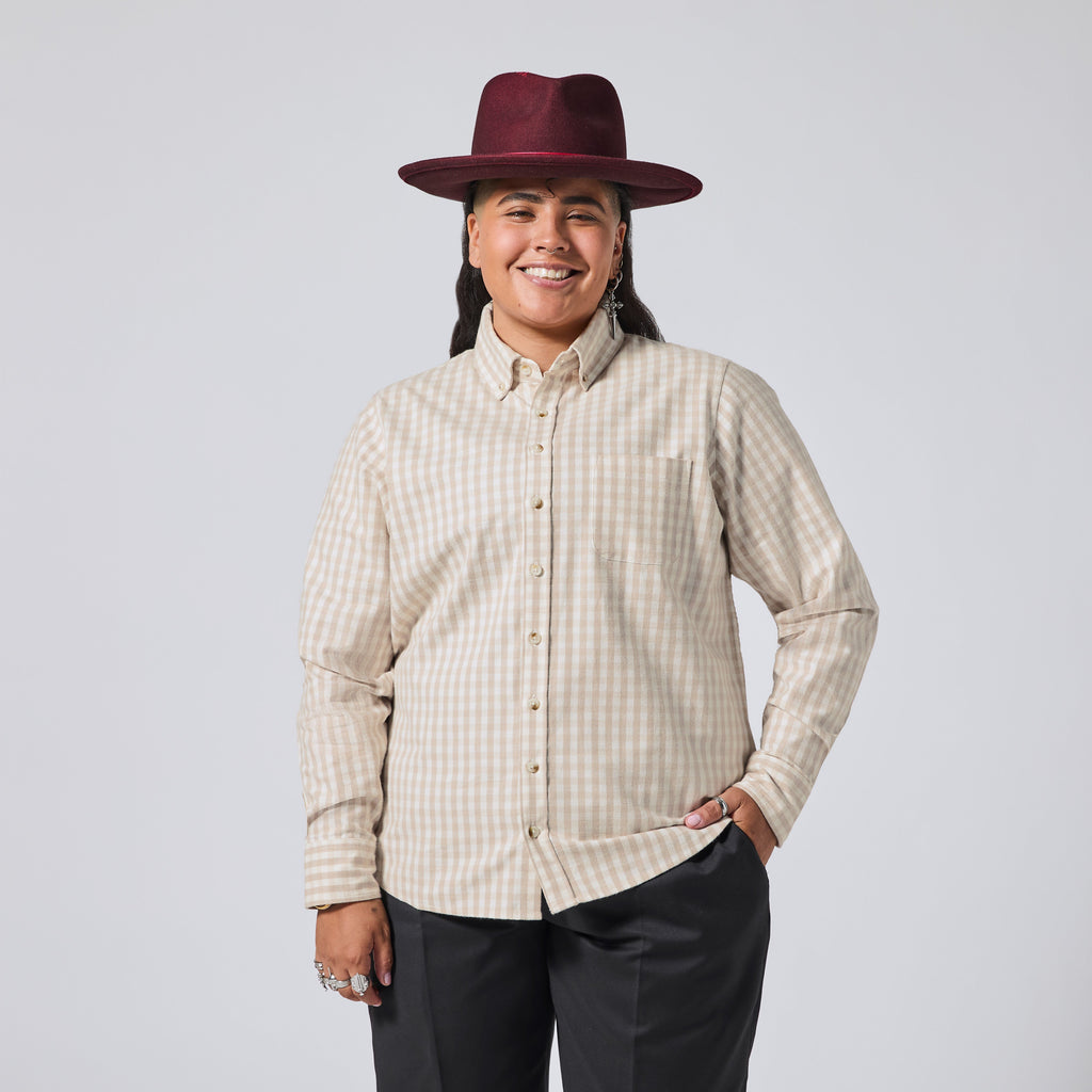Model in a beige and white gingham long-sleeve button-down shirt, paired with dark gray pants and a burgundy wide-brim hat, against a solid light gray background. Color: Cream Check Flannel