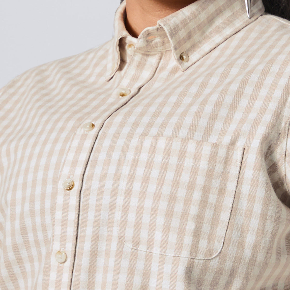 Close-up of a person wearing a beige and white gingham button-down shirt with a chest pocket, showing the collar, buttons, and fabric texture. Color: Cream Check Flannel