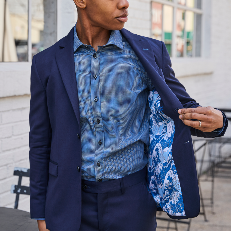 Person wearing a blue suit with a patterned shirt, standing outdoors.
