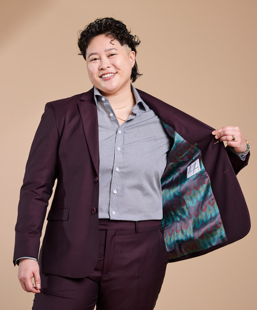 Person wearing a burgundy suit with a colorful lining, standing against a beige background