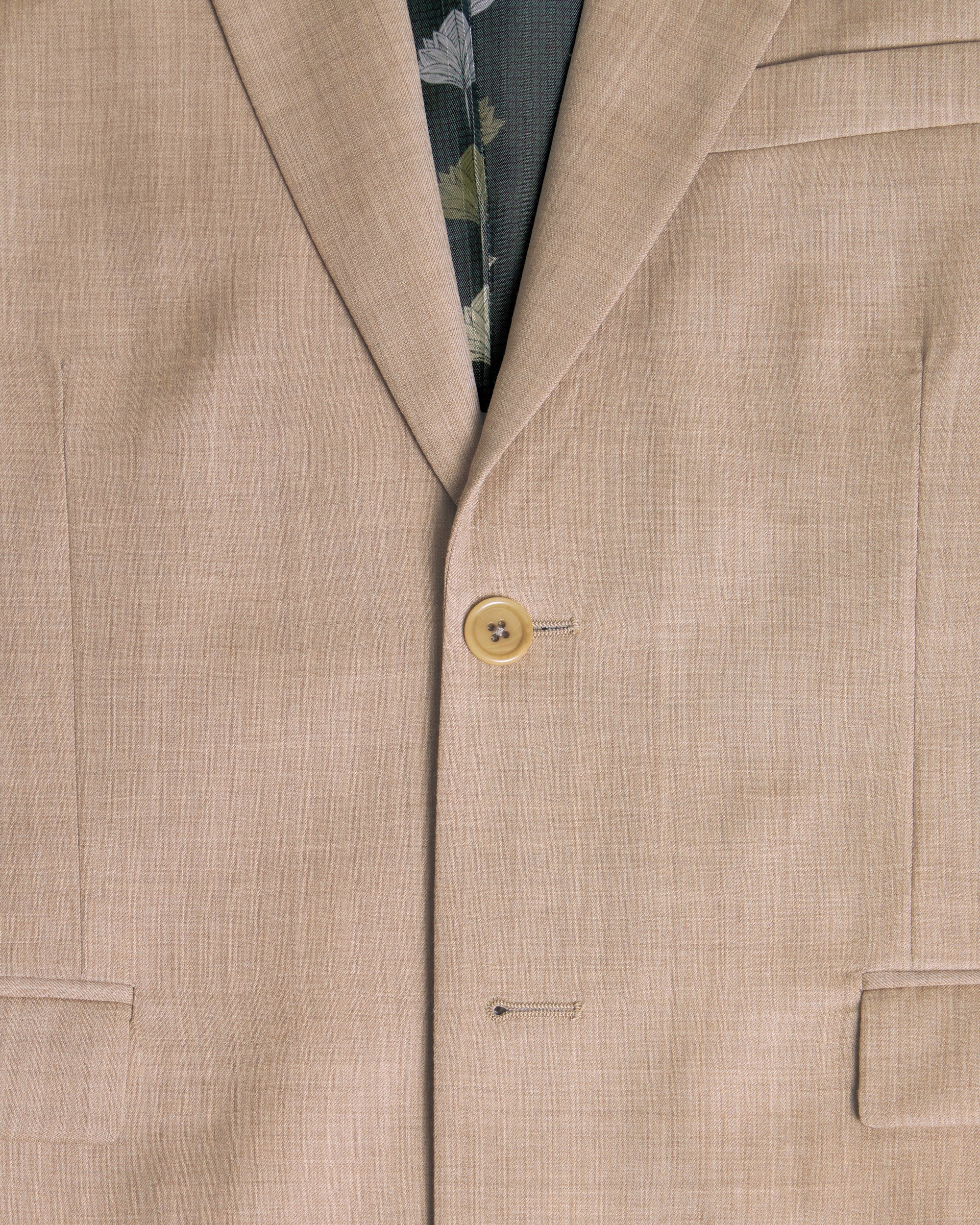 Close-up of a beige suit jacket with a button and floral patterned inner lining. Color: Desert