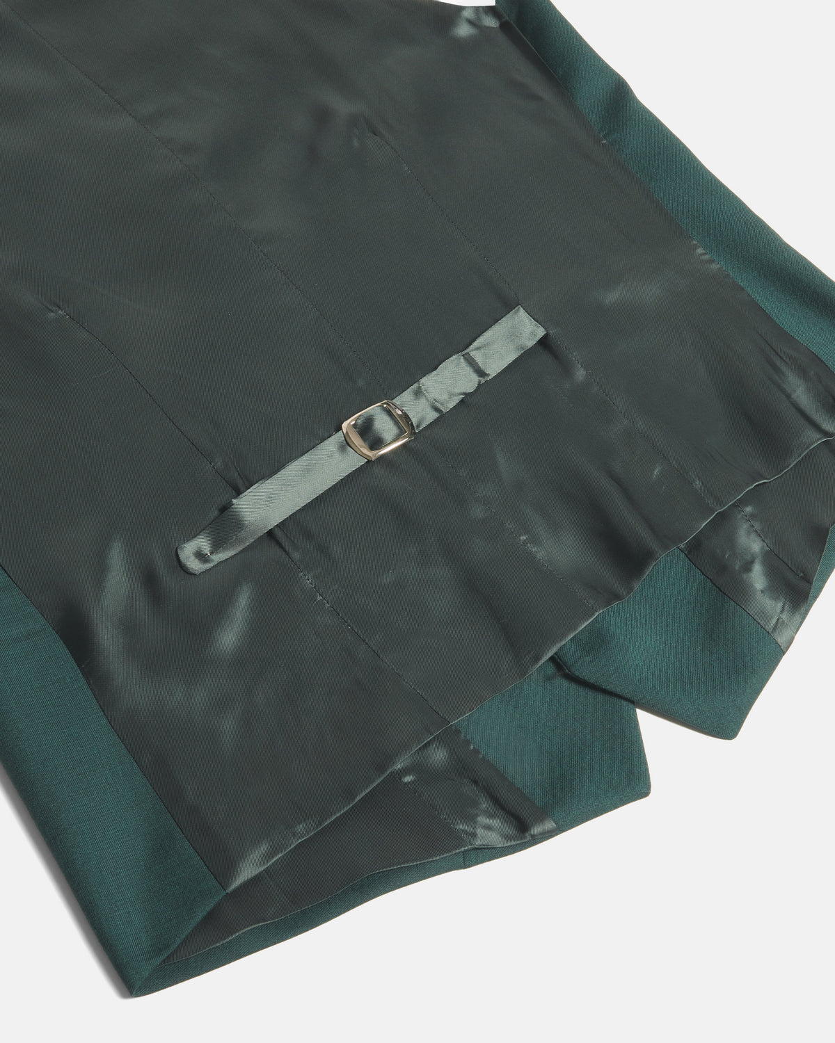 Close-up of a dark green satin garment with a matching fabric strap and small gold-tone buckle detail, photographed on a light gray background. Color: Emerald