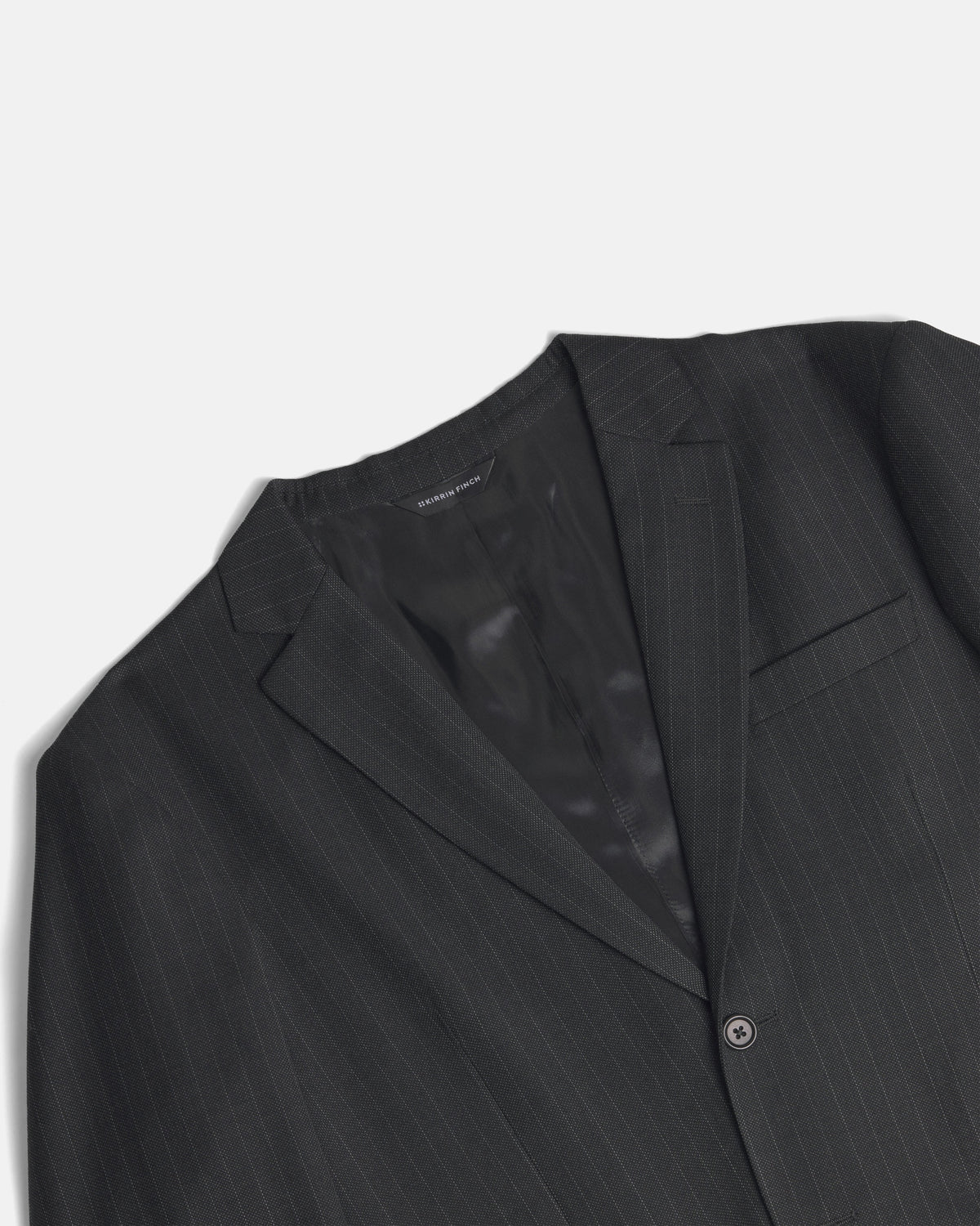 A close-up of a dark charcoal gray pinstripe suit jacket, showing the lapel, inner collar, and a single button closure against a light gray background. Color: Shadow Pinstripe