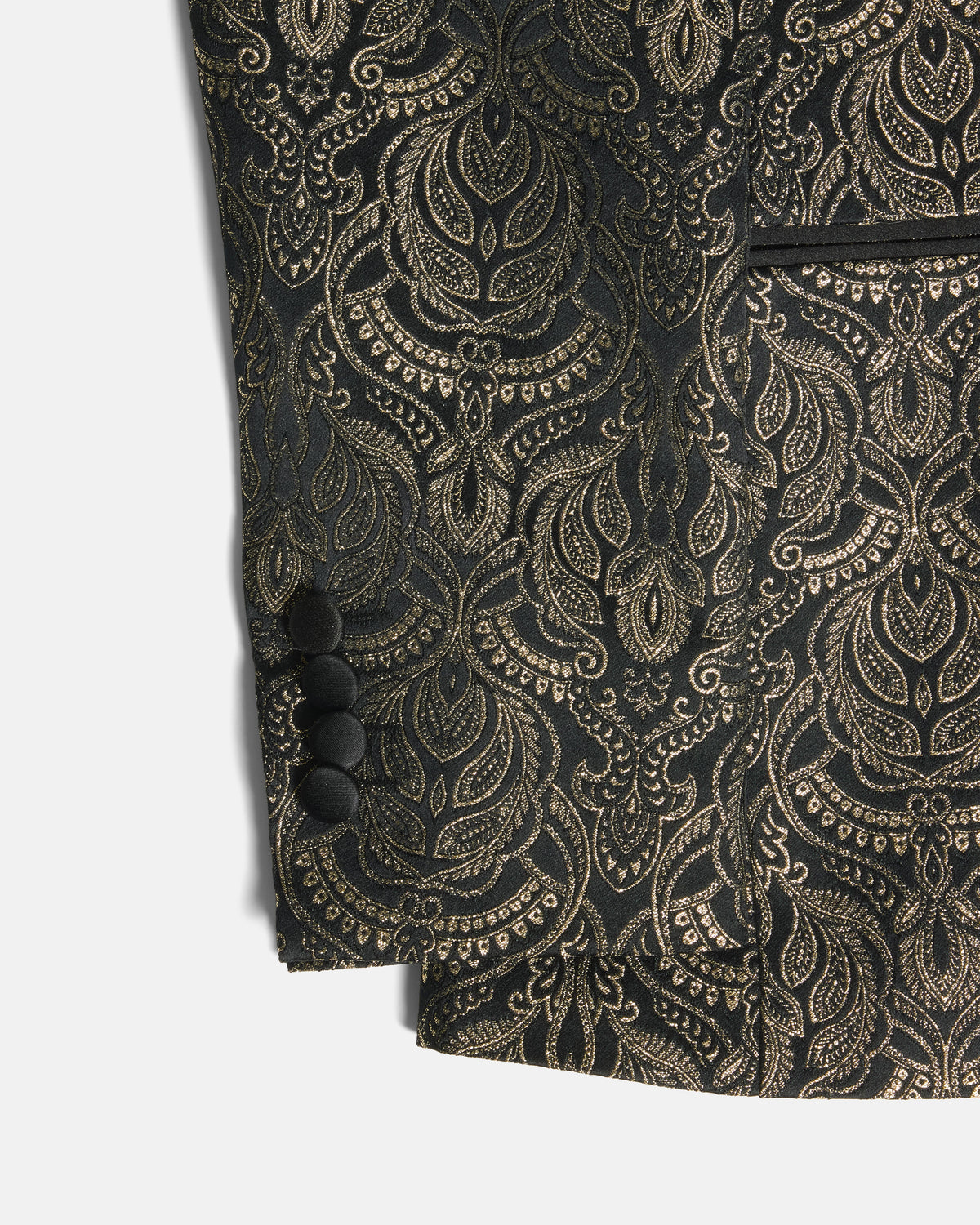 Close-up of a black and gold jacquard fabric garment, showing an ornate paisley pattern, four black buttons on the sleeve cuff, and a pocket edge against a light gray background. Color: Gilded Brocade