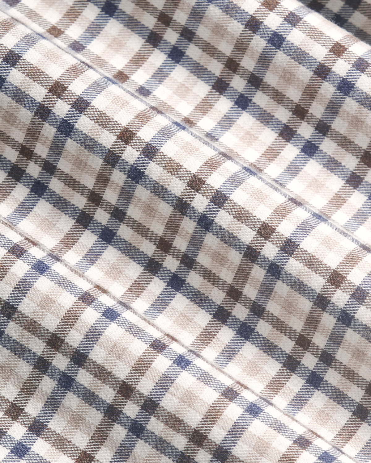 A close-up of a plaid fabric pattern with intersecting diagonal stripes in navy blue, brown, and light beige on an off-white background. Color: Herritage Plaid