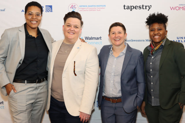 Four people posing together in front of a branded backdrop with logos.