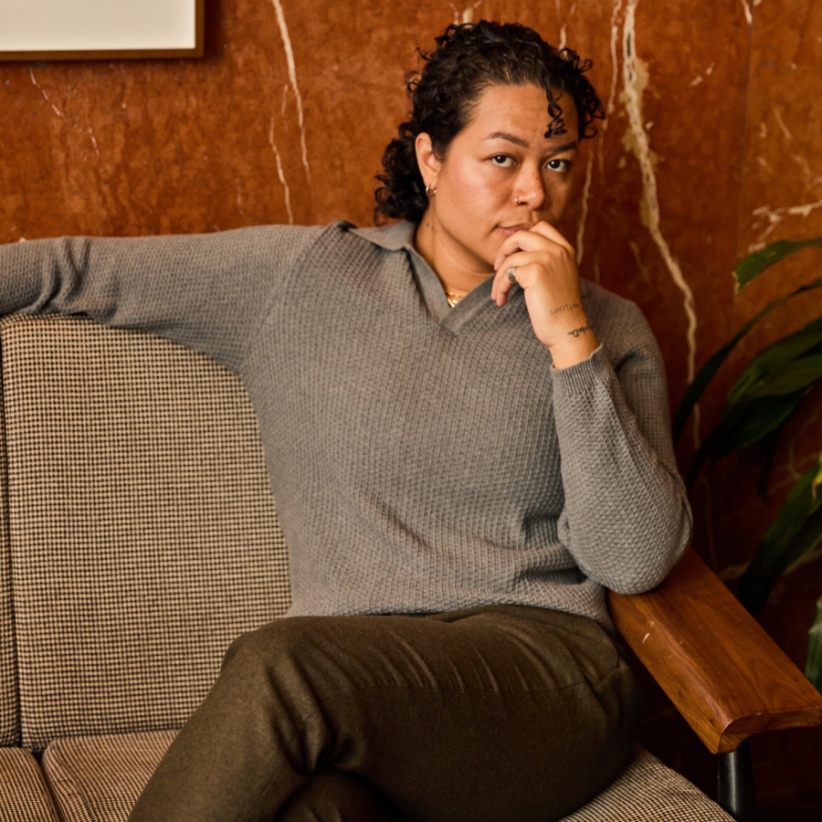 Person in a grey sweater sitting on a couch with a textured wall in the background.