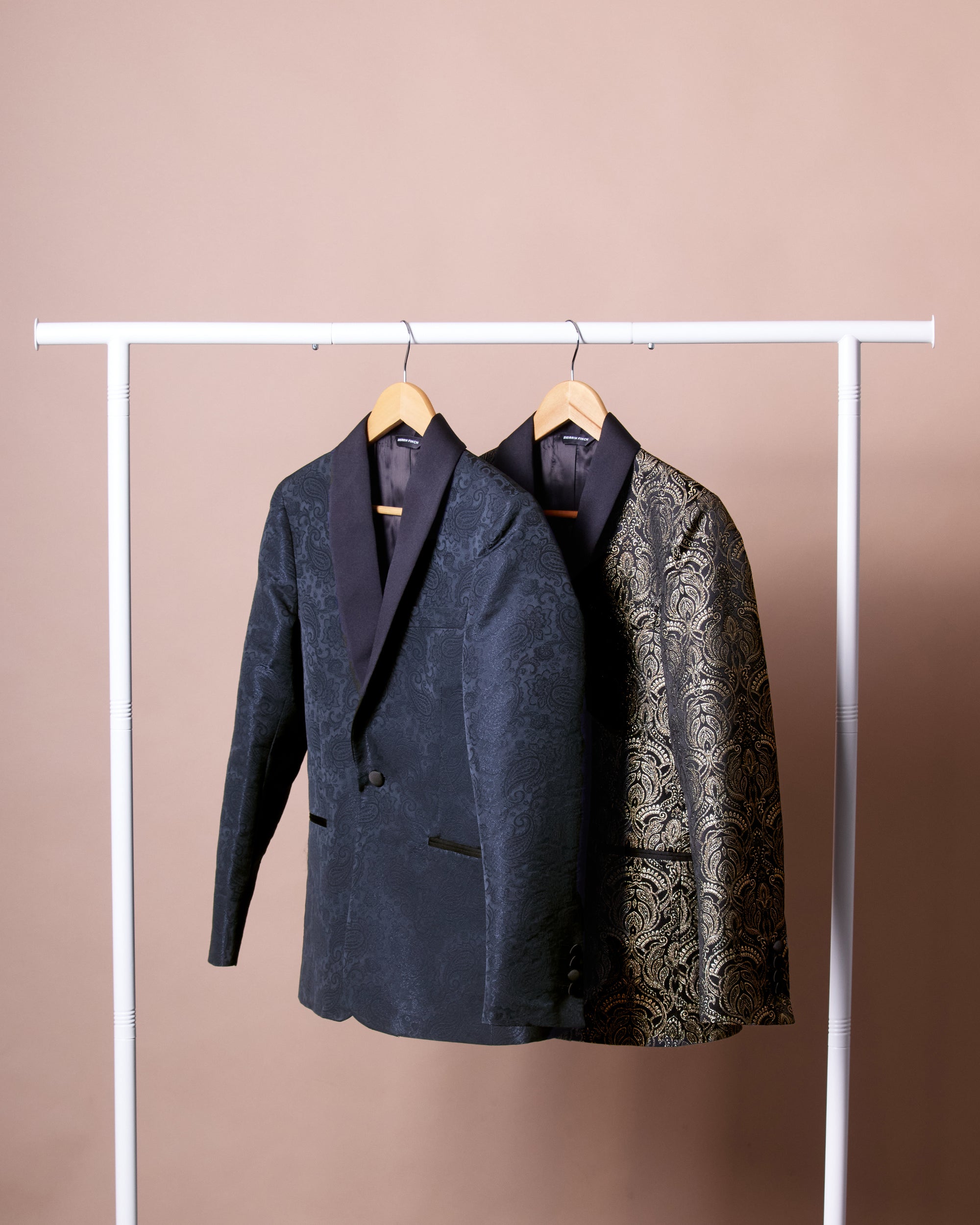 Two blazer, one dark blue with floral pattern and one black with floral pattern, on hangers against a beige background. Color: Sapphire Brocade