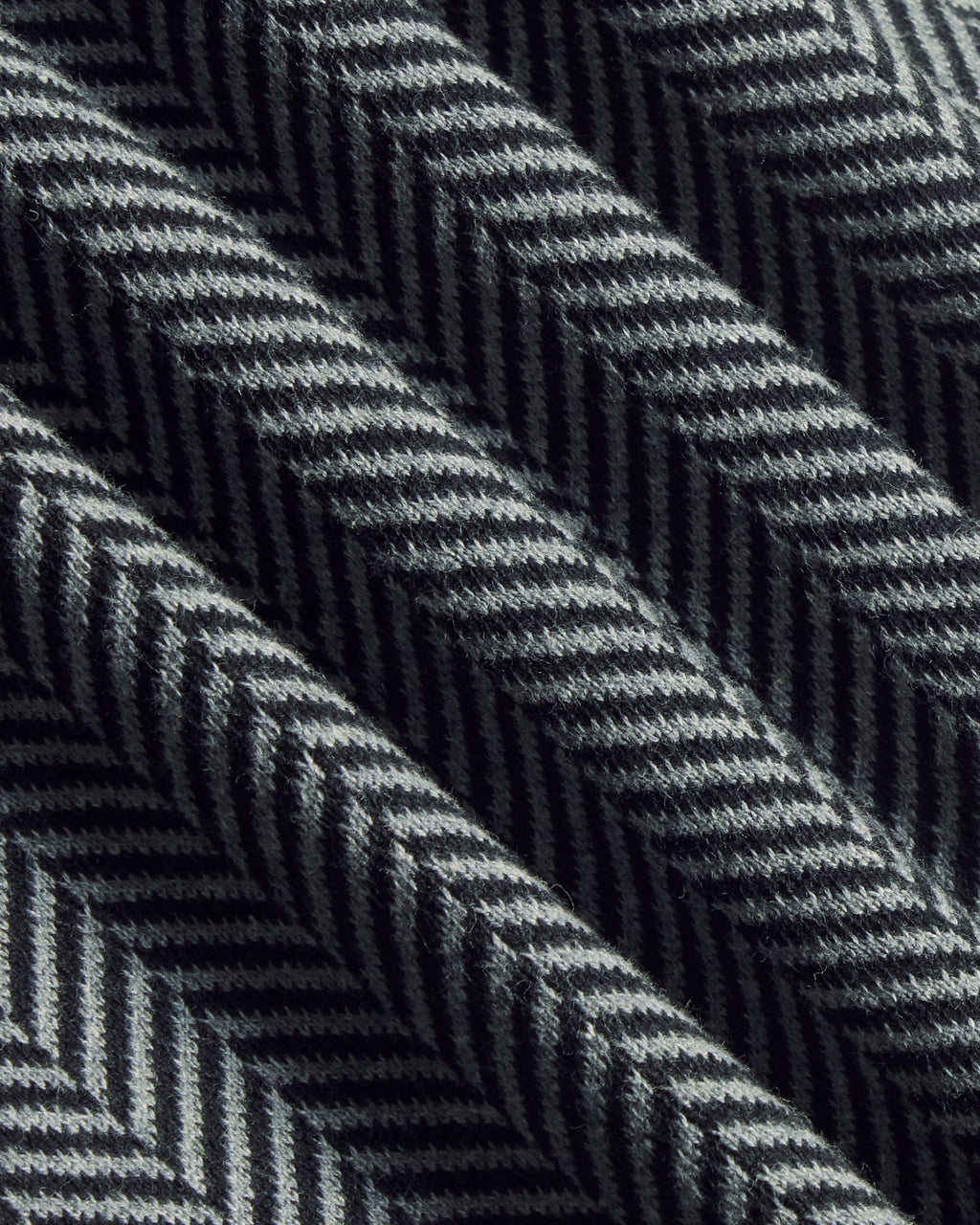 A close-up of a woven fabric with a dark gray and black herringbone pattern, showing the texture and diagonal folds. Color: Inkstone Herringbone