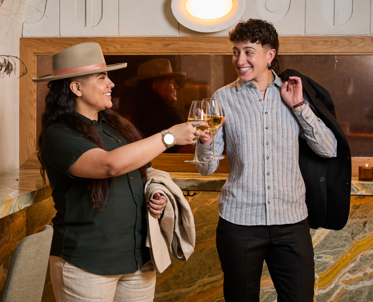 Two people in a warm, indoor setting with one holding a glass of wine.