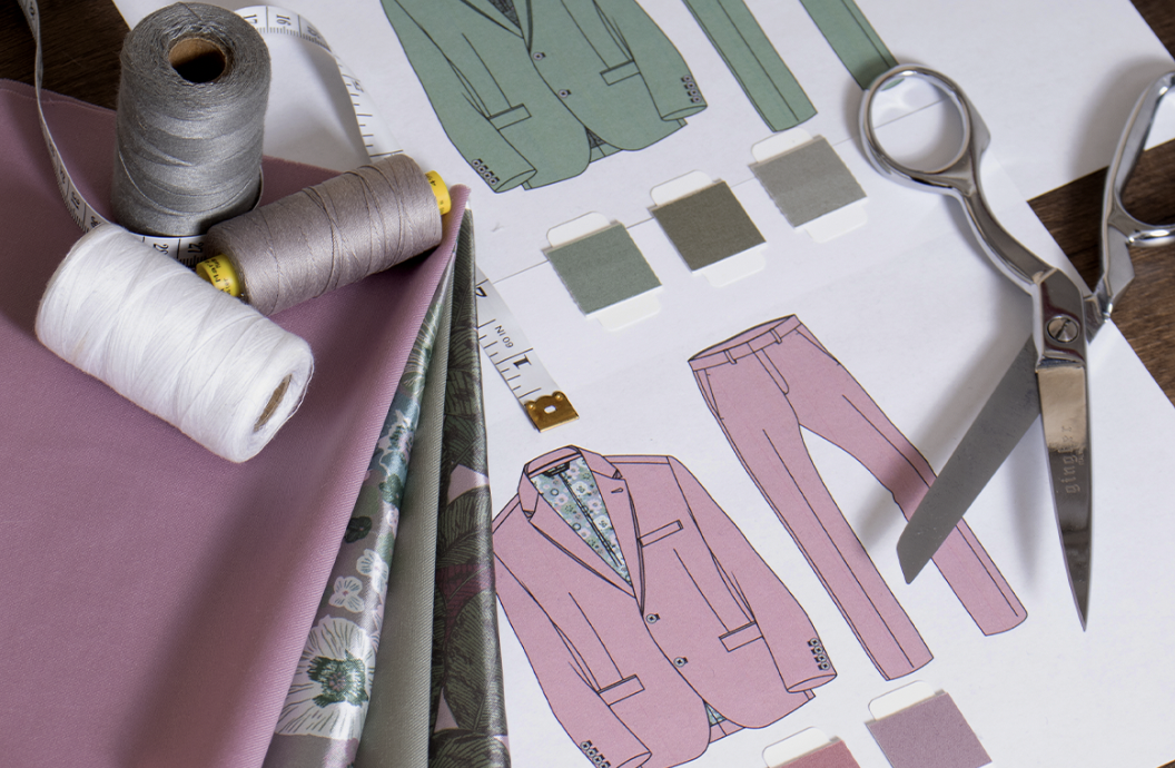 Fabric swatches, scissors, and thread on a table with fashion design illustrations.