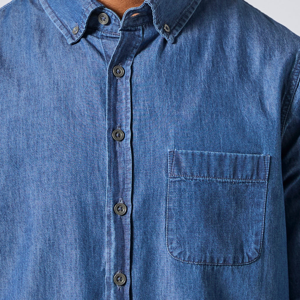 Close-up of a blue denim button-down shirt with a chest pocket, shown on a model. Color: Medium Wash Denim