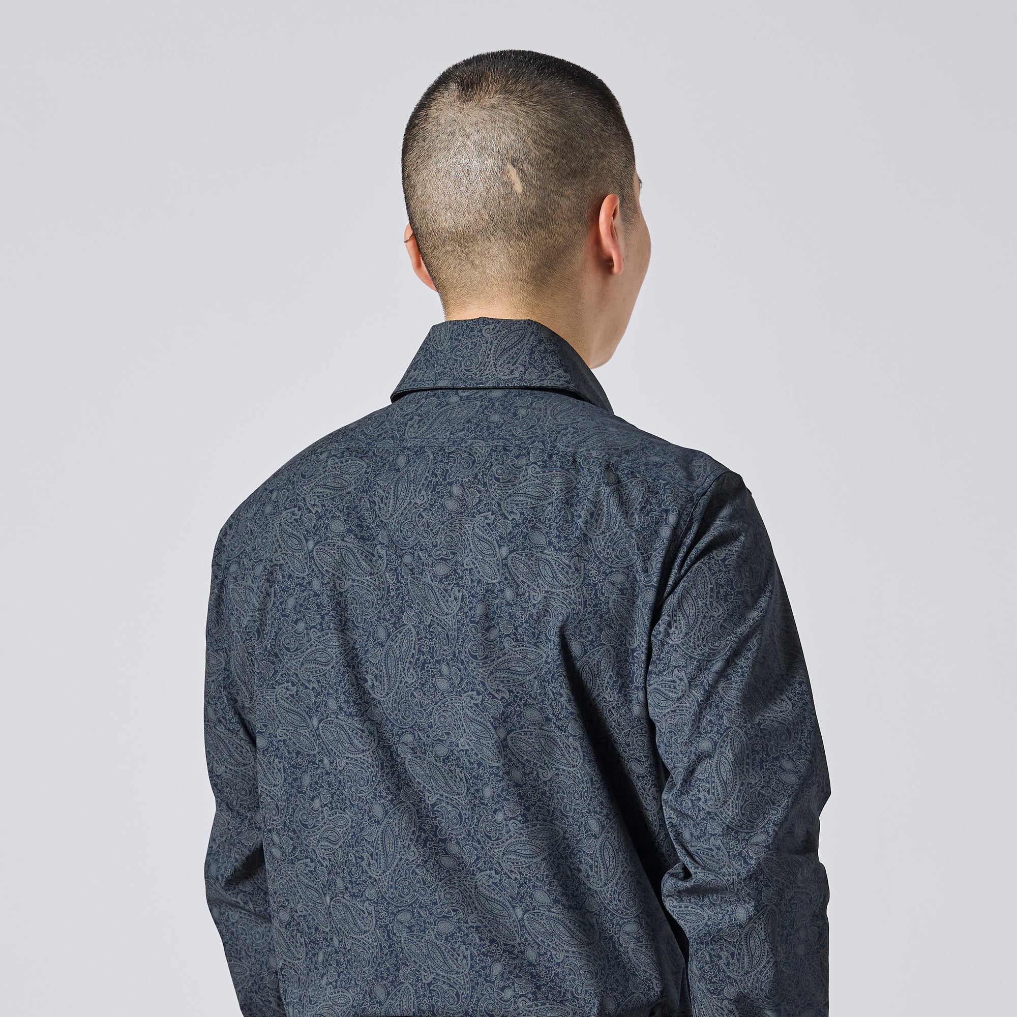 Model viewed from behind wearing a dark blue patterned long-sleeve shirt against a light gray studio background. Color: Midnight Paisley
