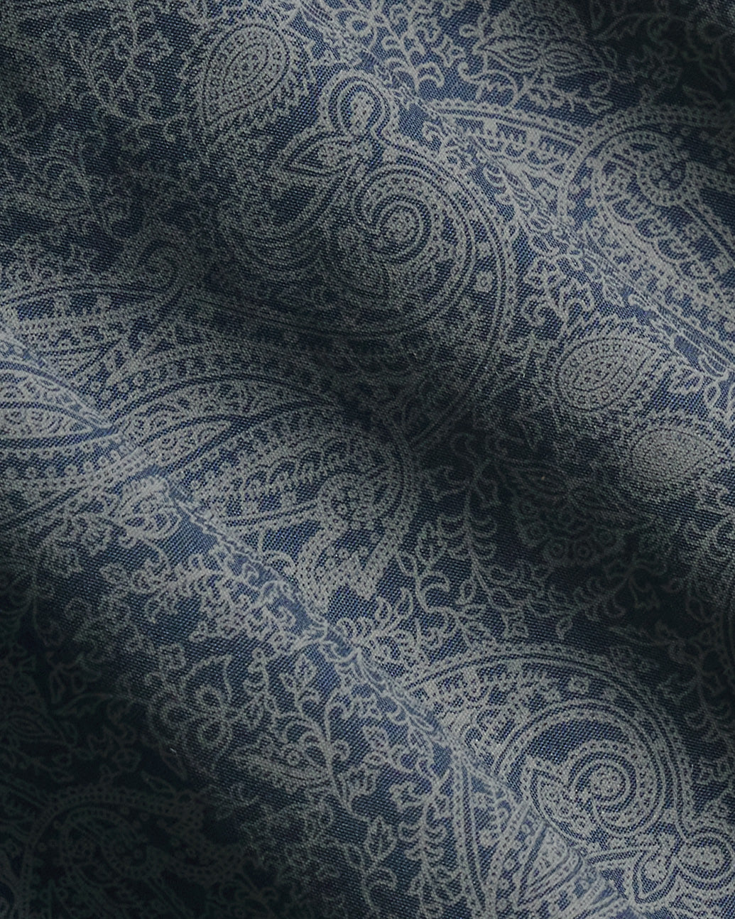 A close-up of a navy blue fabric with a detailed off-white paisley pattern, showing soft folds and shadows. Color: Midnight Paisley