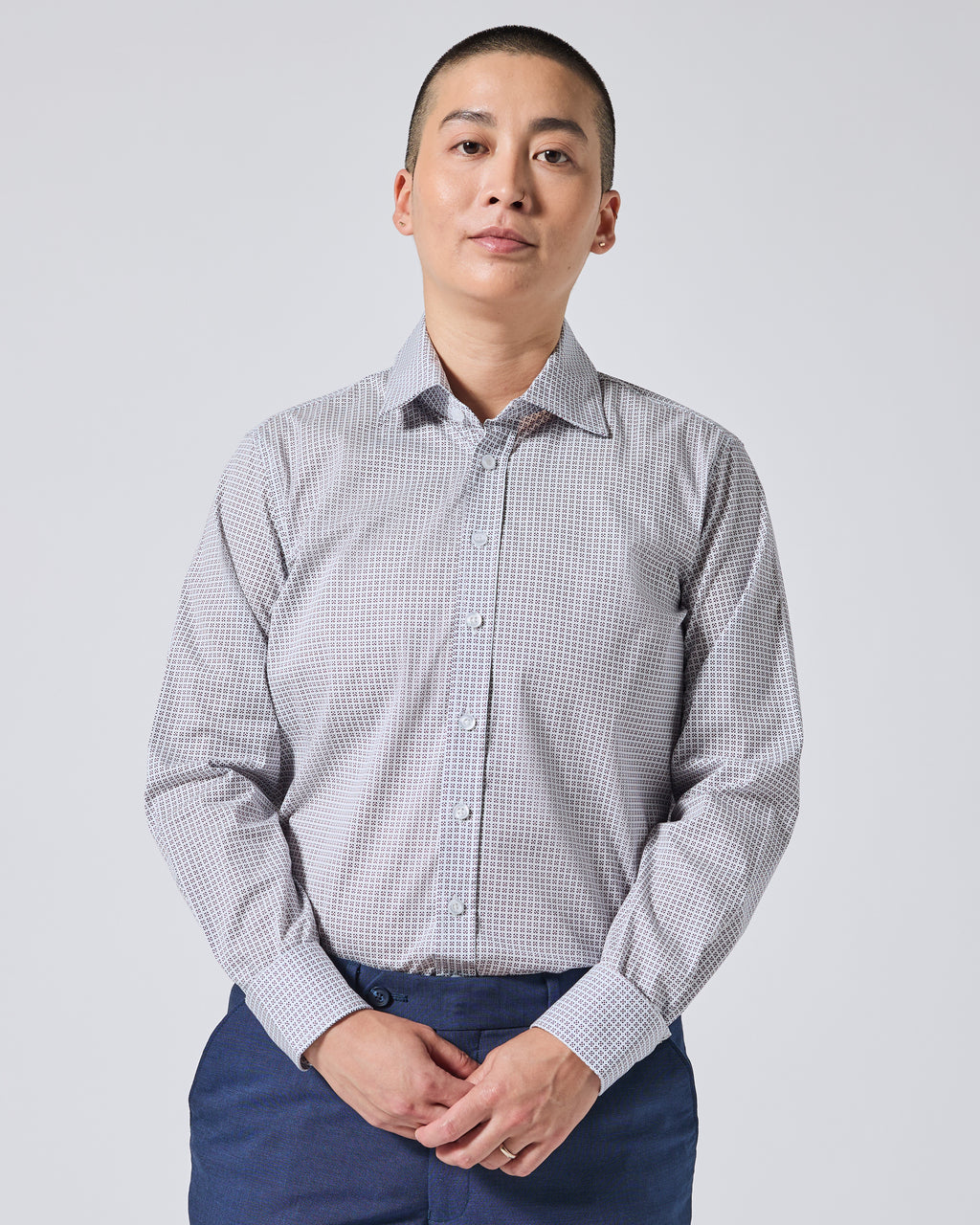 A person wearing a long-sleeve button-up shirt paired with navy blue trousers, standing against a light gray studio background. Color: Navy Rosette