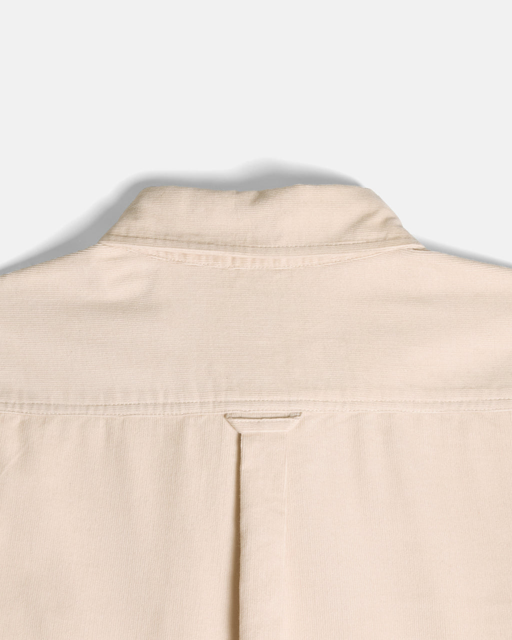 Close-up of the back collar and upper back of a light beige or cream-colored shirt, showing fabric texture and stitching against a plain light gray background.  Color: Oatmeal
