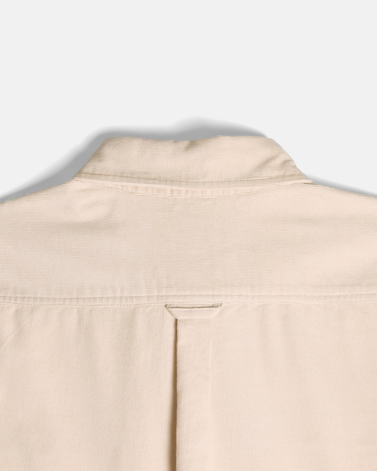 Close-up of the back collar and upper back of a light beige or cream-colored shirt, showing fabric texture and stitching against a plain light gray background.  Color: Oatmeal