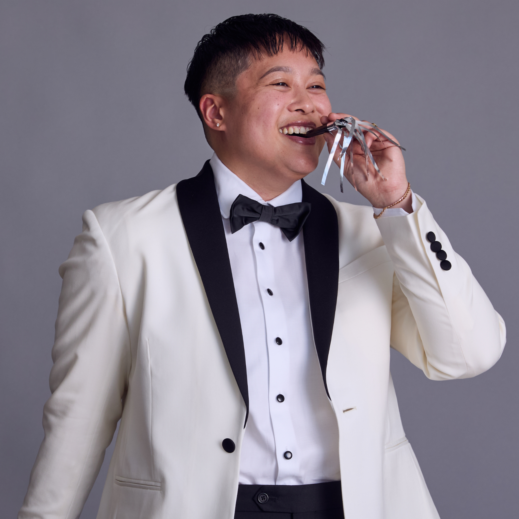 Model in white tuxedo and black bowtie blowing into a party blower.