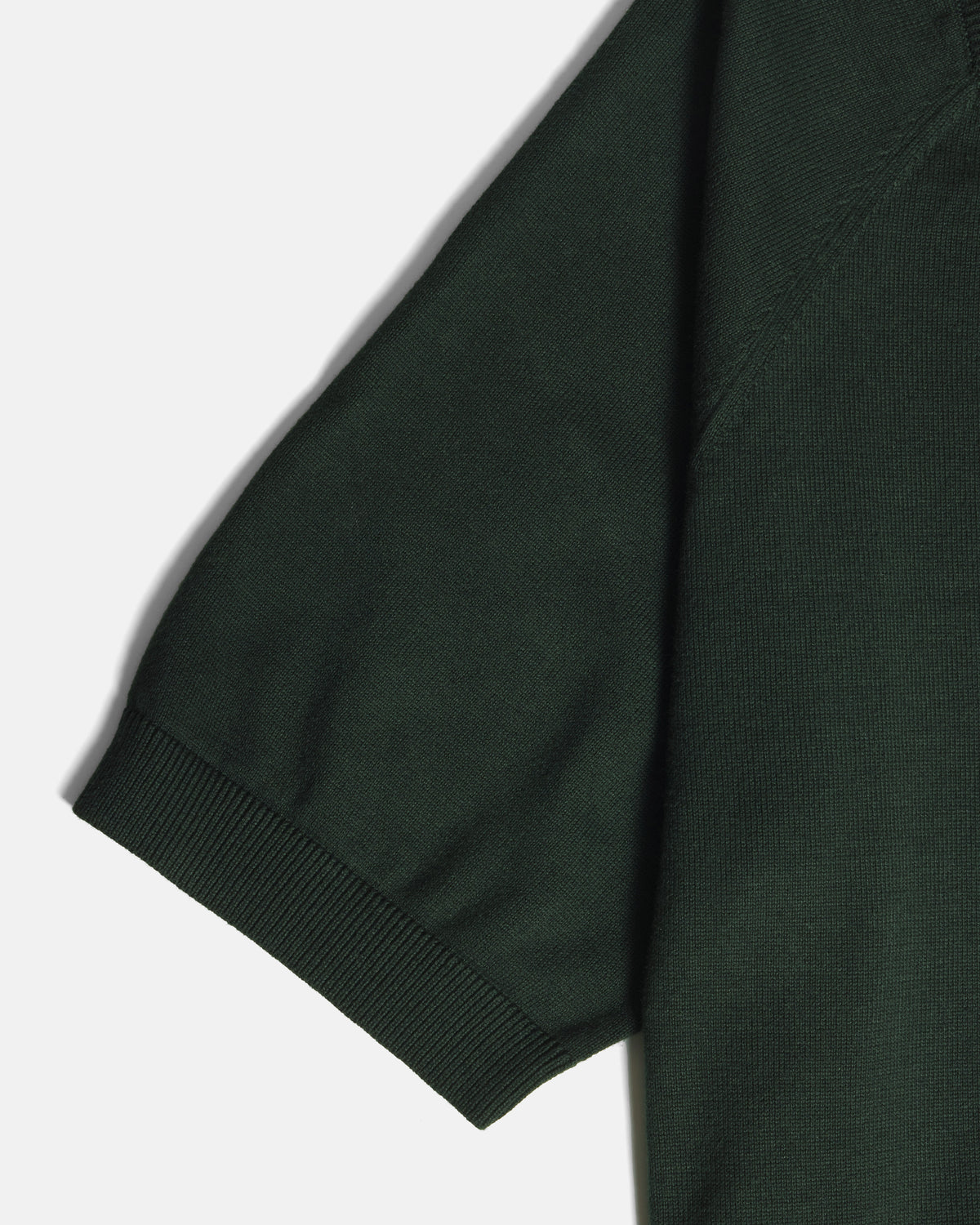Close-up of a dark forest green short-sleeve knit garment, showing the ribbed cuff and part of the sleeve against a light gray background. Color: Evergreen