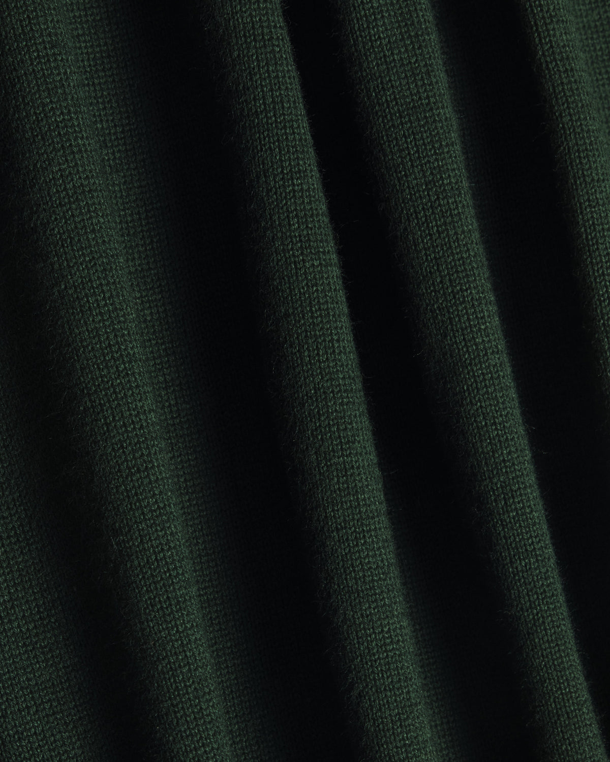 A close-up of dark forest green knit fabric with soft vertical folds showing the texture and weave. Color: Evergreen
