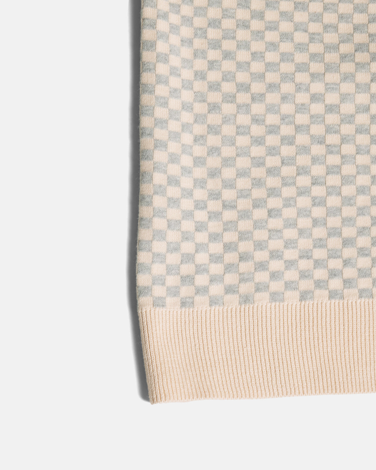 Close-up of a ribbed knit fabric with a small checkerboard pattern in light gray and cream, finished with a cream ribbed hem. Color: Saltstone Checker