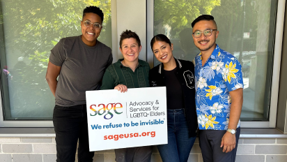 Four Kirrin FInch team members holding a sign for Sage, an organization advocating for LGBTQ+ rights.