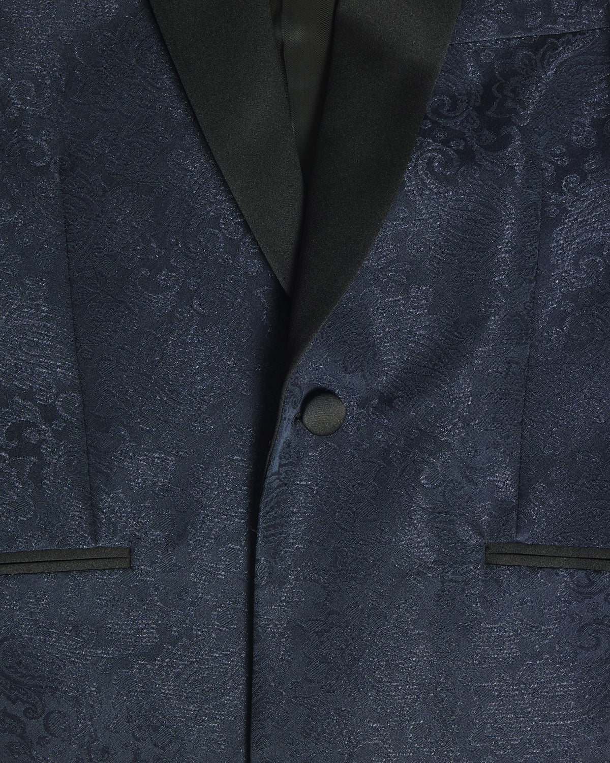 Close-up of a navy blue patterned suit jacket with black satin lapels and a matching dark button. Color: Sapphire Brocade
