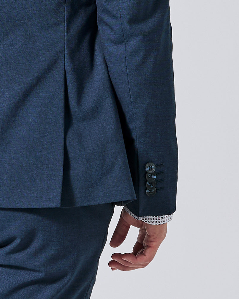 Close-up of an Atlantic blue suit jacket and matching trousers, showing the sleeve with three dark buttons and a white patterned cuff lining, worn by a model against a light gray background. Color: Atlantic Blue