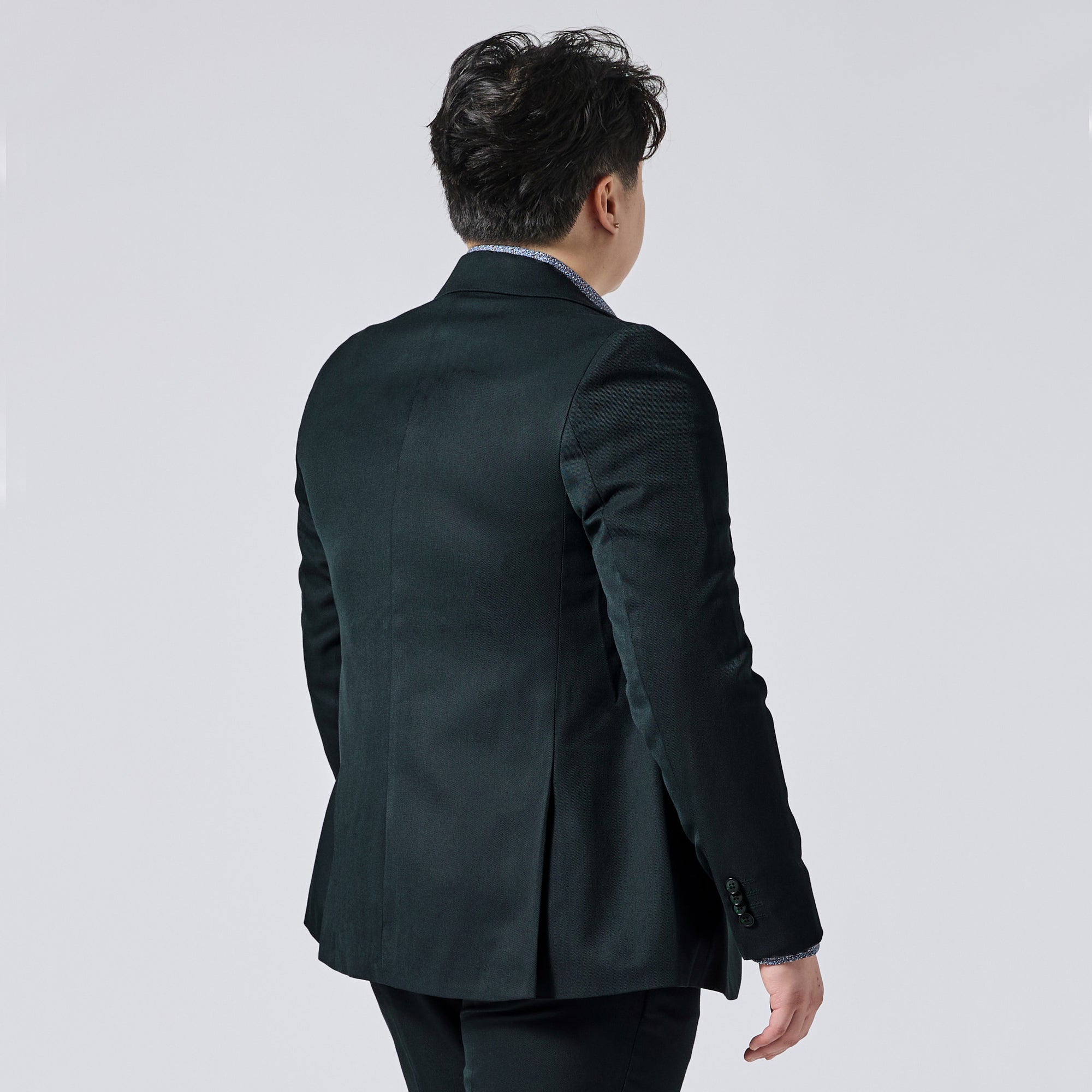 Person viewed from behind wearing a Phantom Green Twill blazer over a light blue collared shirt, set against a plain light gray studio background. Color: Phantom Green Twill
