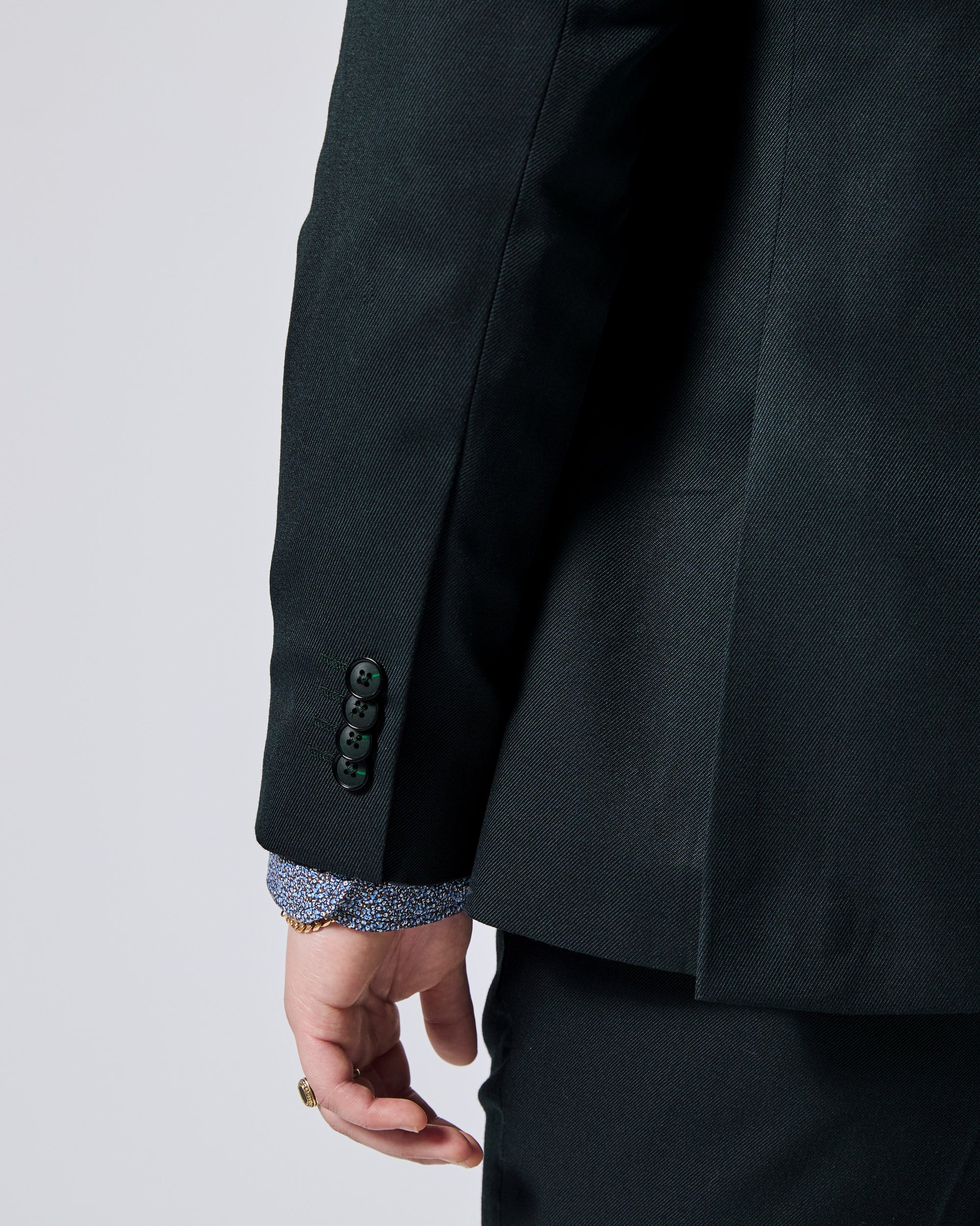 Close-up of a Green Phantom Twill Scout suit jacket sleeve with three dark buttons, showing a patterned blue and white shirt cuff underneath, worn by a model. Color: Phantom Green Twill