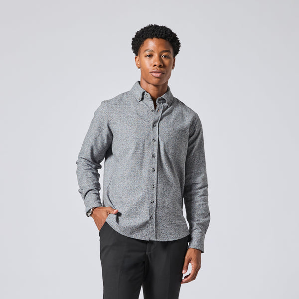 Model wearing a gray long-sleeve button-down shirt with a subtle textured pattern, paired with black trousers, standing against a light gray studio background. Color: Static Flannel