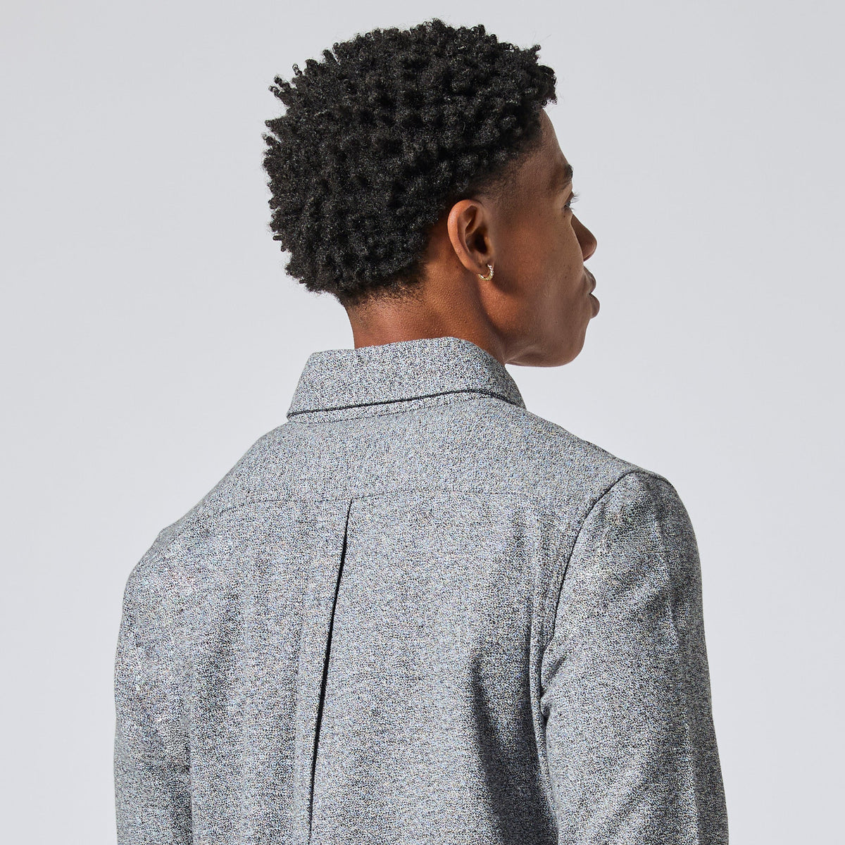 Model with short, curly black hair is shown from the back wearing a textured gray collared shirt jacket against a light gray studio background. Color: Static Flannel