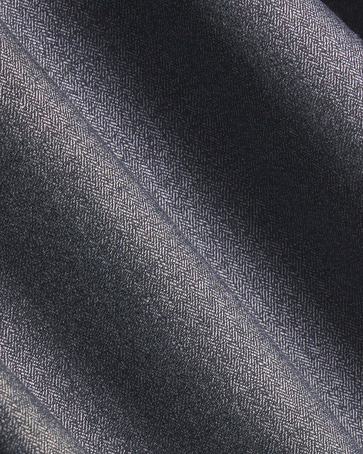 A close-up of dark charcoal gray herringbone fabric with a subtle woven texture and soft diagonal folds. Color: Steel Marl Herringbone