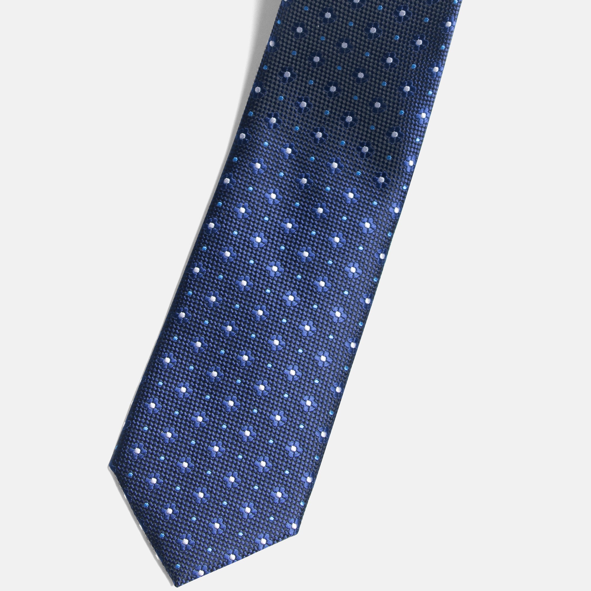 Blue tie with white polka dots on a light gray background. Color: Micro Daisy
