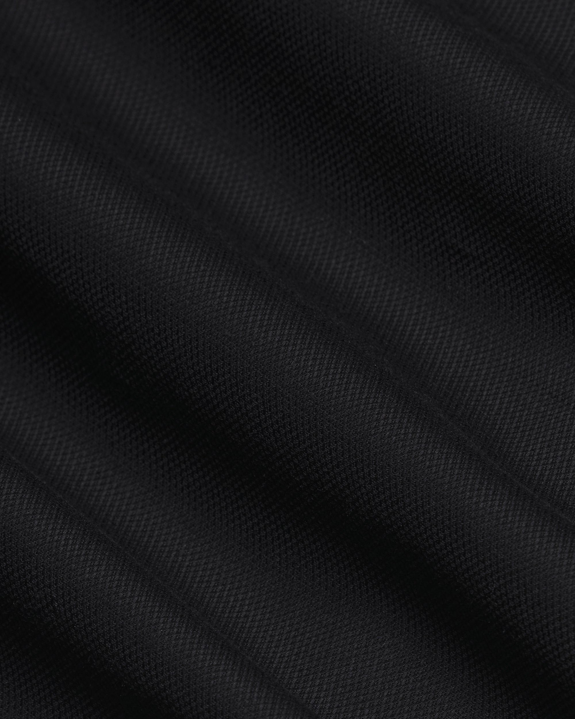 A close-up of black textured fabric with a fine woven pattern and soft diagonal folds. Color: Black