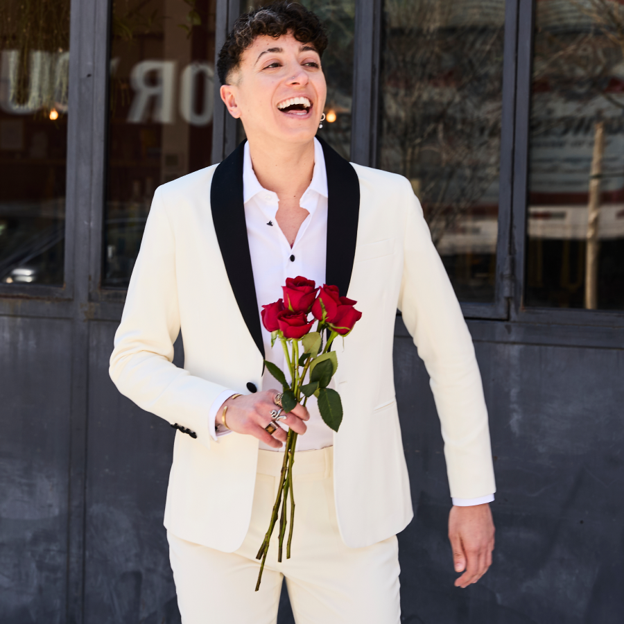 Model wearing the ivory Kirrin tuxedo holding red roses outdoors.